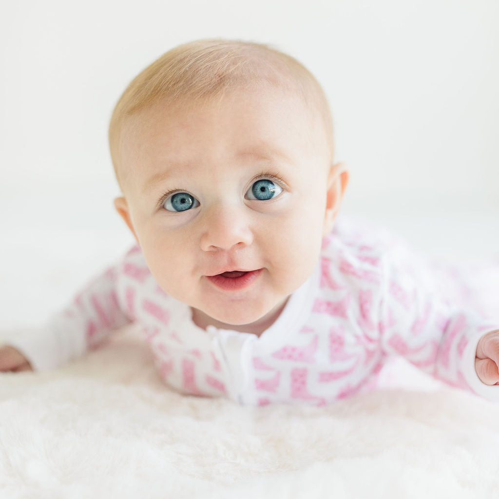 Baby with blue eyes wearing a pink and white cowboy boot pajamas on a white background