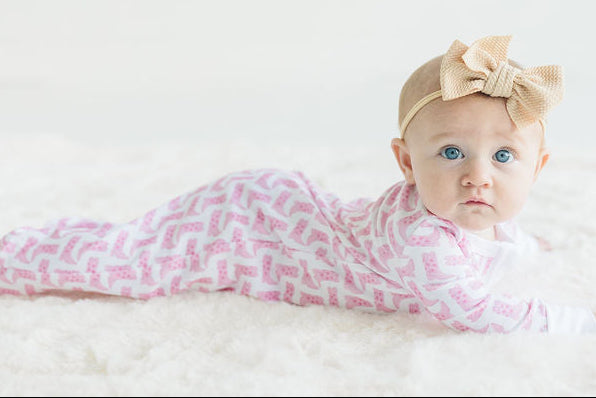 Baby in a pink cowboy boot pajamas with a bow on a white background